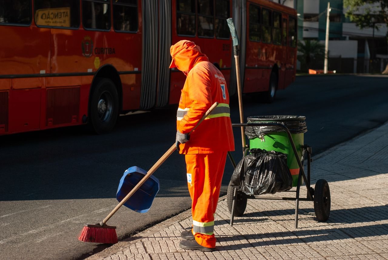 The Art of Drawing Readers In: Your attractive post title goes here Street cleaner in bright orange uniform sweeping sidewalk near public bus in city setting.