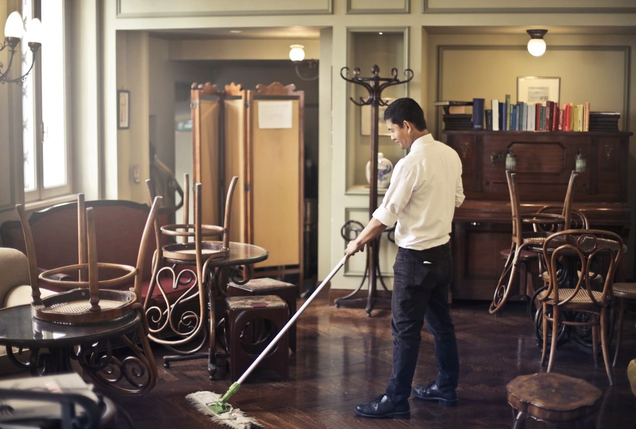 Mastering the First Impression: Your intriguing post title goes here Side view of young ethnic male in uniform cleaning floor with mop while working in retro styled restaurant